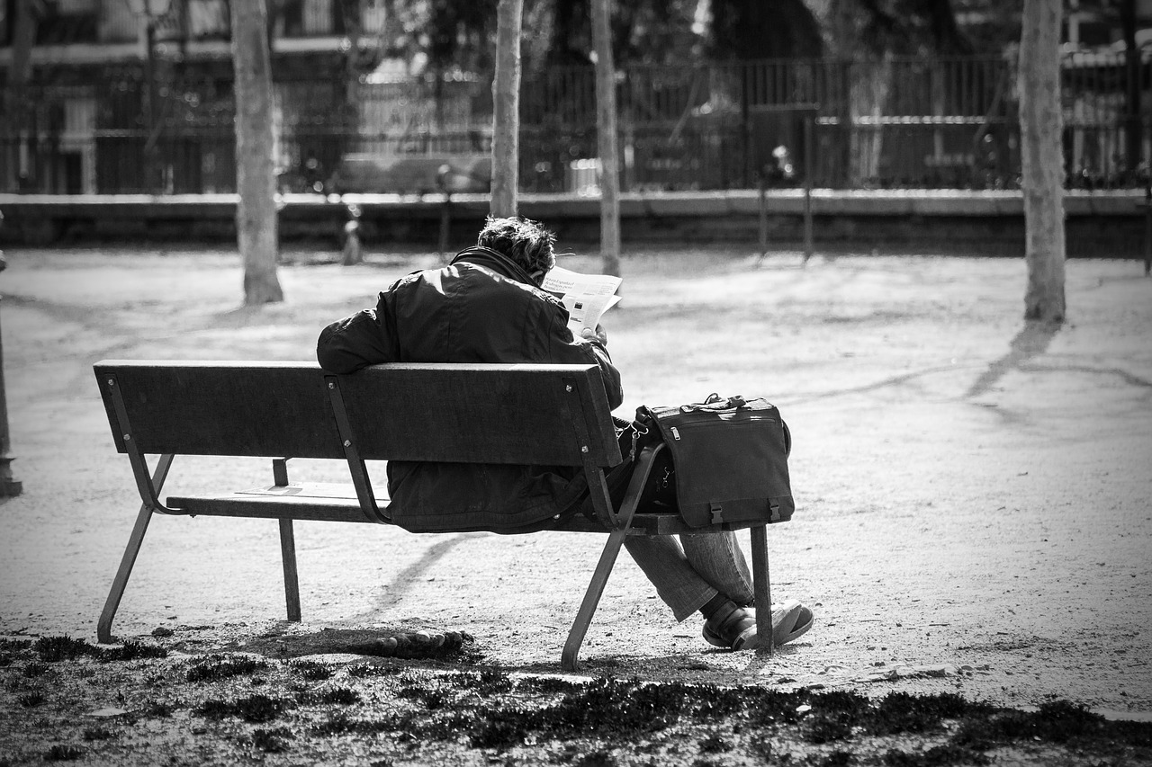 man on a bench park reading the newspaper free photo