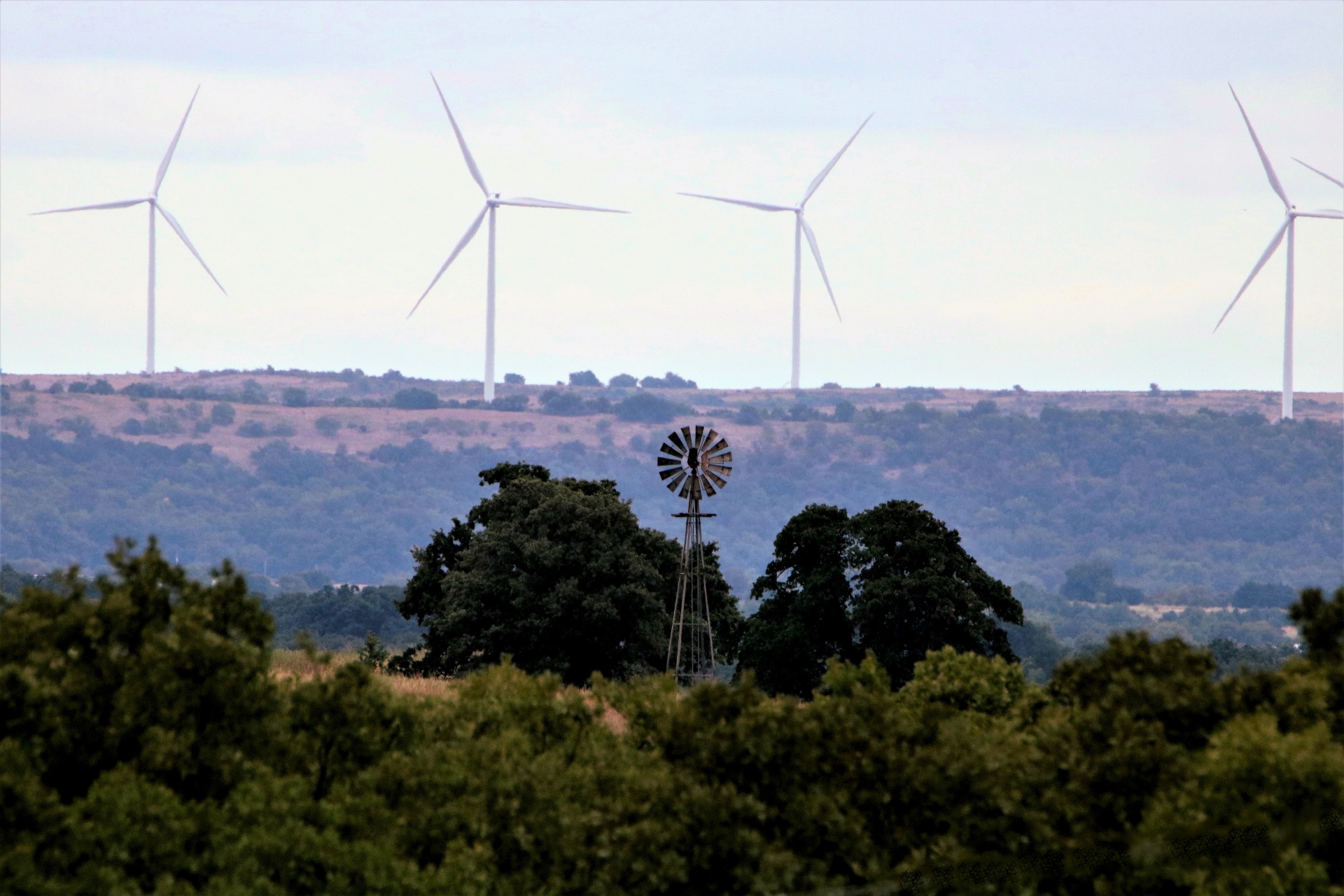 landscape shot old abandoned wind mill standing tall among green trees today's new wind turbines along ridge background windmills of yesterday and today free photo