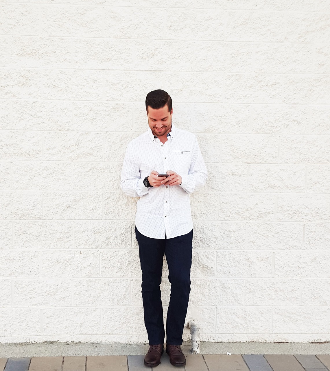 young man looking at phone brick wall free photo